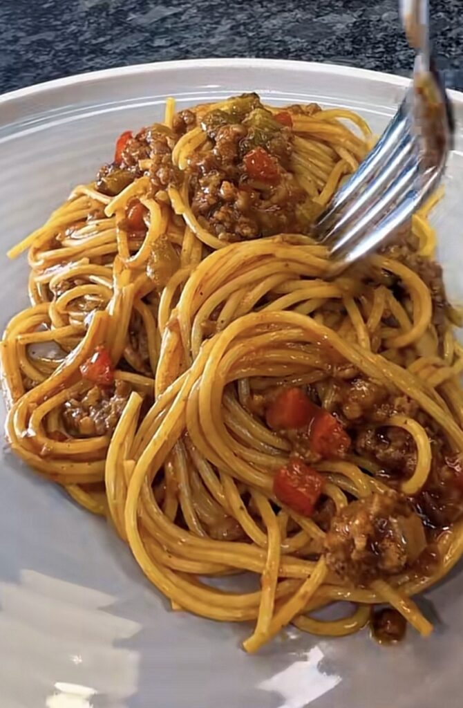 Close-up of dirty spaghetti with a fork, coated in Cajun meat sauce with ground beef, sausage, and red bell peppers