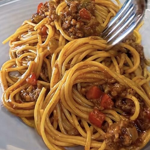 Dirty spaghetti recipe served on a plate with a fork, Cajun pasta with ground beef, sausage, and bell peppers