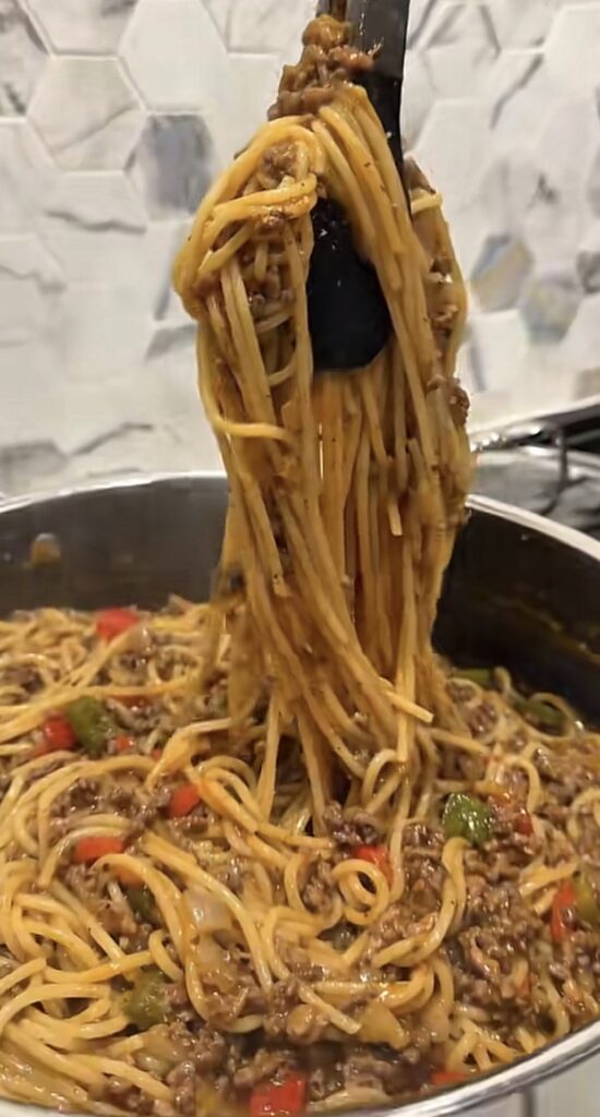 Dirty spaghetti being lifted from a pan, showing the deep brown Cajun pasta coated in seasoned beef and sausage drippings