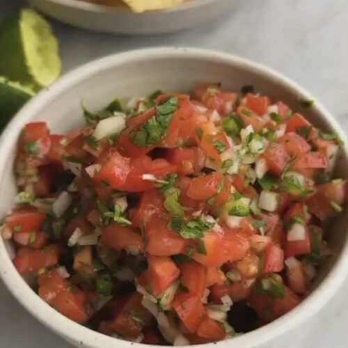 authentic pico de gallo recipe in a white bowl with Roma tomatoes, cilantro, white onion, serrano pepper, and lime - restaurant style pico de gallo